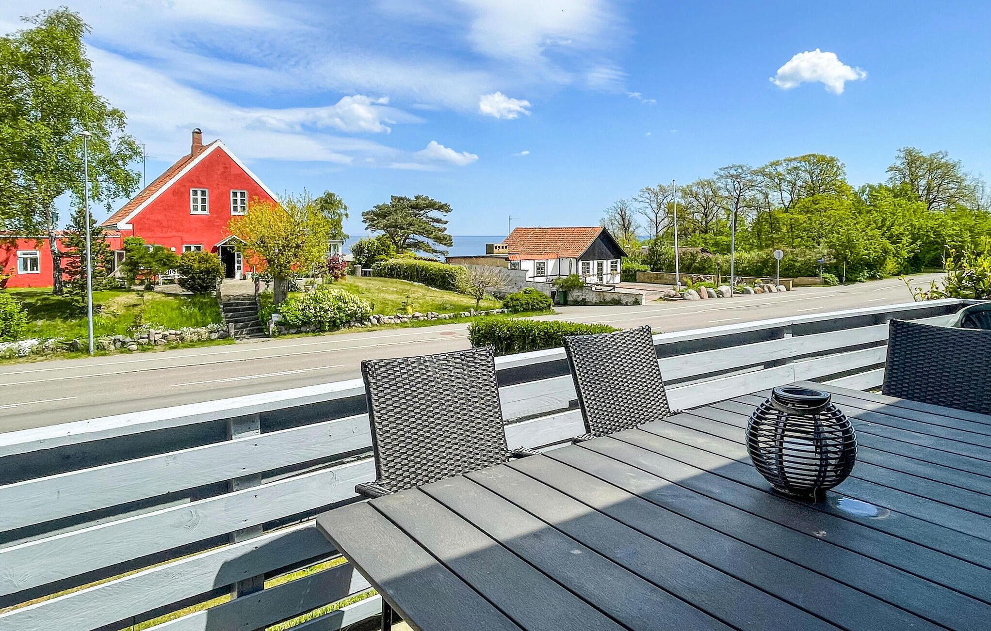 En träaltan med utemöbler, ett rött hus och utsikt över havet.