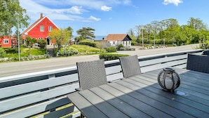 Een houten terras met tuinmeubilair, een rood huis en uitzicht op zee.