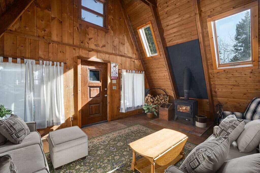 Interior acogedor de una cabaña con paredes de madera, chimenea, sofá, mesa y puerta.