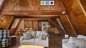 A cozy attic room with a sofa, chairs, and a dining table. There is a staircase leading to another level. - A-Frame Home,2mi from Mt.Snow w/Wood Burning Stove (Dover)