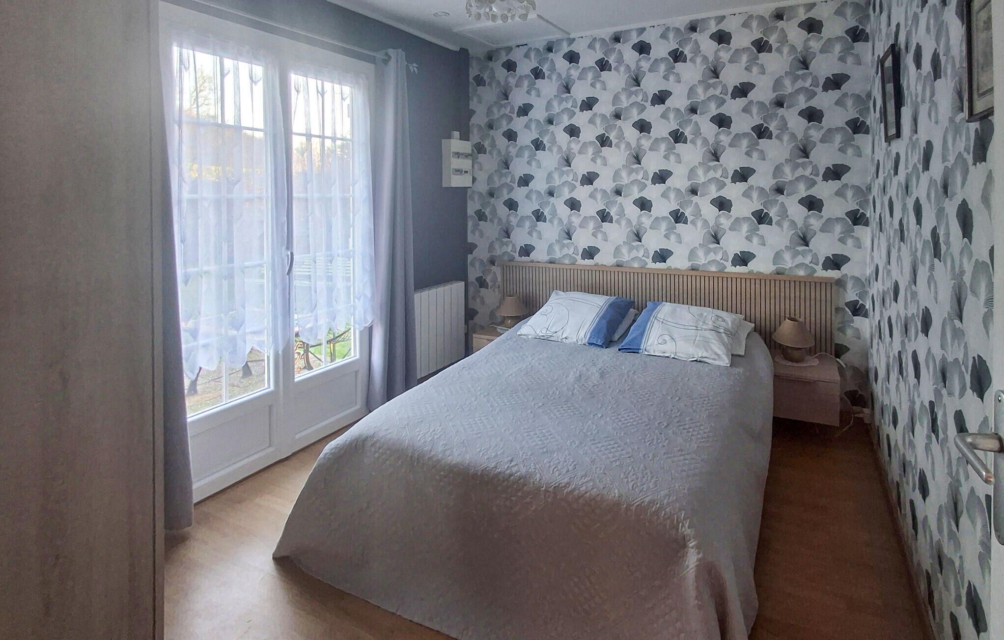 Un dormitorio con cama, mesita de noche, lámpara y ventana con cortinas.