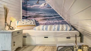 A bedroom with a bed, a nightstand, a lamp, a vase with dried plants, and a decorative wall mural of the ocean. - Ferienhaus 12 in Kirchheim (Kirchheim)