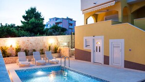 Une piscine avec des chaises longues, un mur en pierre et un bâtiment à la façade jaune.