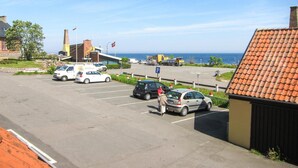 Um estacionamento com vários carros, um edifício com telhado de telhas vermelhas e vista para o mar.