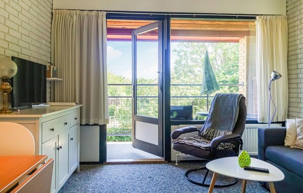 Relax in this cozy space with a balcony door leading to an outdoor area, featuring a comfortable chair, a small table, and a TV on a cabinet.