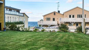 A coastal residential area with two-story houses, a car parked in front, and a view of the sea.