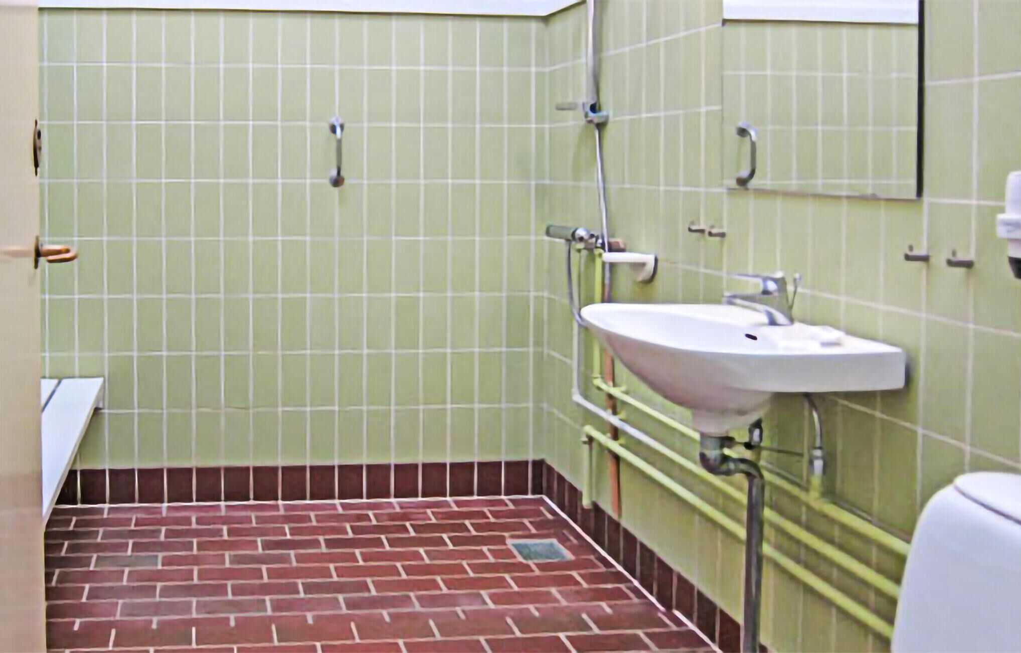 Ein Badezimmer mit grünen Fliesenwänden, einem weißen Waschbecken und einem roten Ziegelboden.