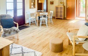 A cozy living room with a wooden floor, a round dining table with chairs, a sofa, and a small ottoman.