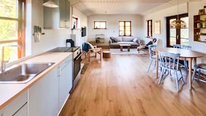 Et moderne køkken med vask, komfur og skabe, et spiseområde med bord og stole, og en opholdsstue med sofa og sofabord.