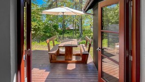 En træterrasse med et picnicbord og stole, en parasol og udsigt over det grønne område.