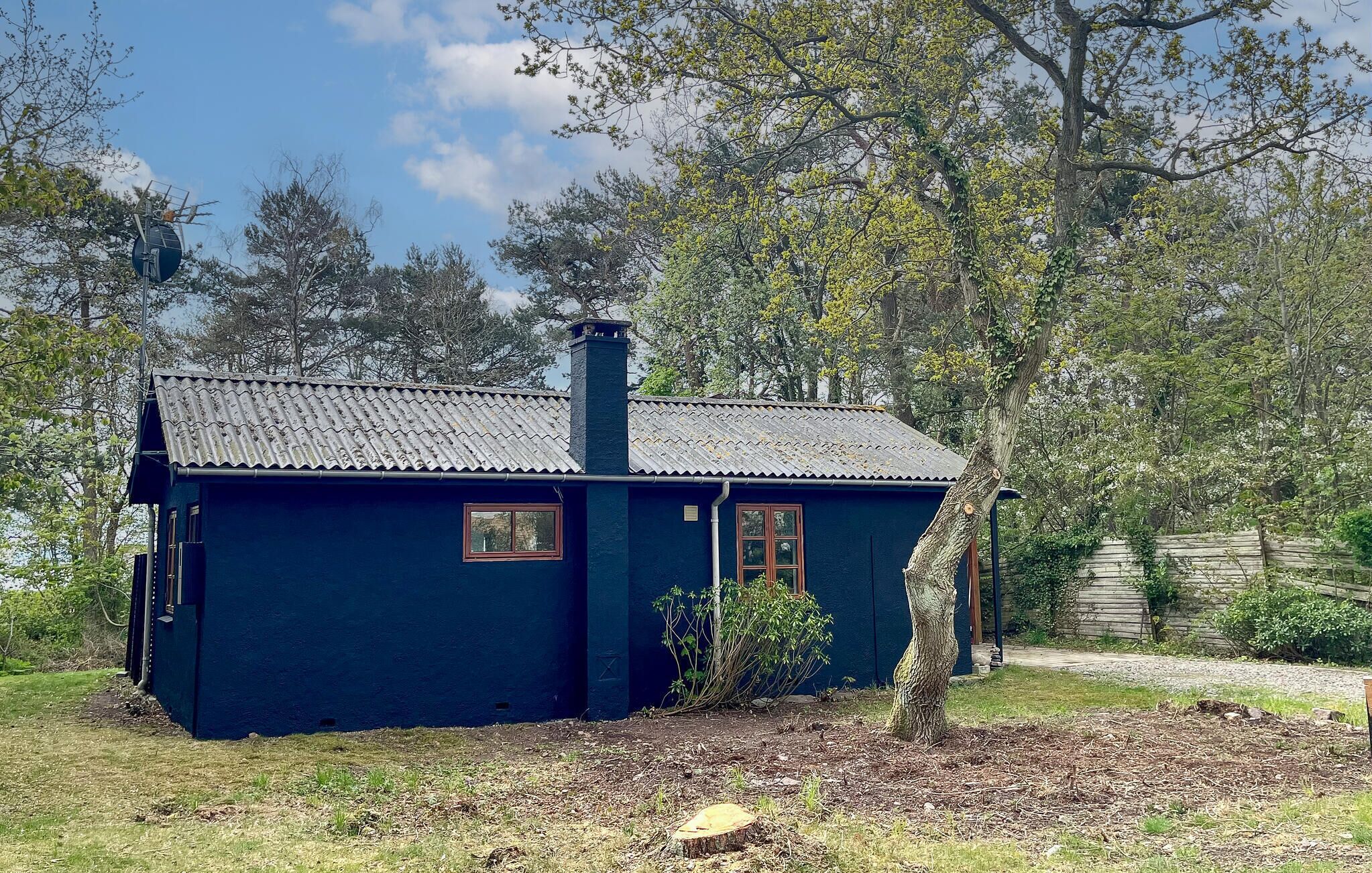 Une petite maison à un seul étage, à l’extérieur d’un bleu foncé, avec une cheminée et une petite fenêtre.