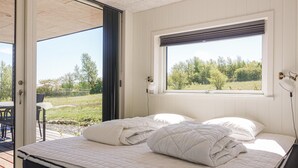 Une chambre avec un lit, une fenêtre donnant sur un espace verdoyant, une porte menant à un espace extérieur et une lampe fixée au mur.