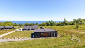 Un bâtiment moderne de style cabane, doté d’une grande terrasse et offrant une vue sur l’océan.