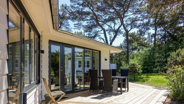 Ein modernes Haus mit Terrasse, großen Glasfenstern und Gartenmöbeln.