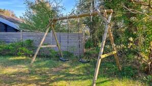 Ein Schaukelstuhl aus Holz im Garten, mit einem Holzzaun und Grünpflanzen im Hintergrund.