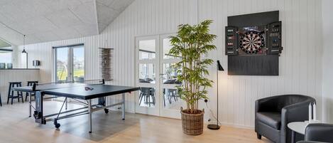 Een moderne woonkamer met een tafeltennistafel, een dartbord en een potplant.
