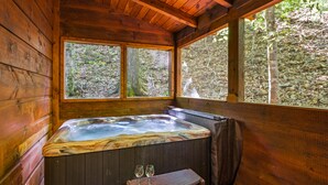 Una baita in legno con idromassaggio, due finestre e una panca con bicchieri.