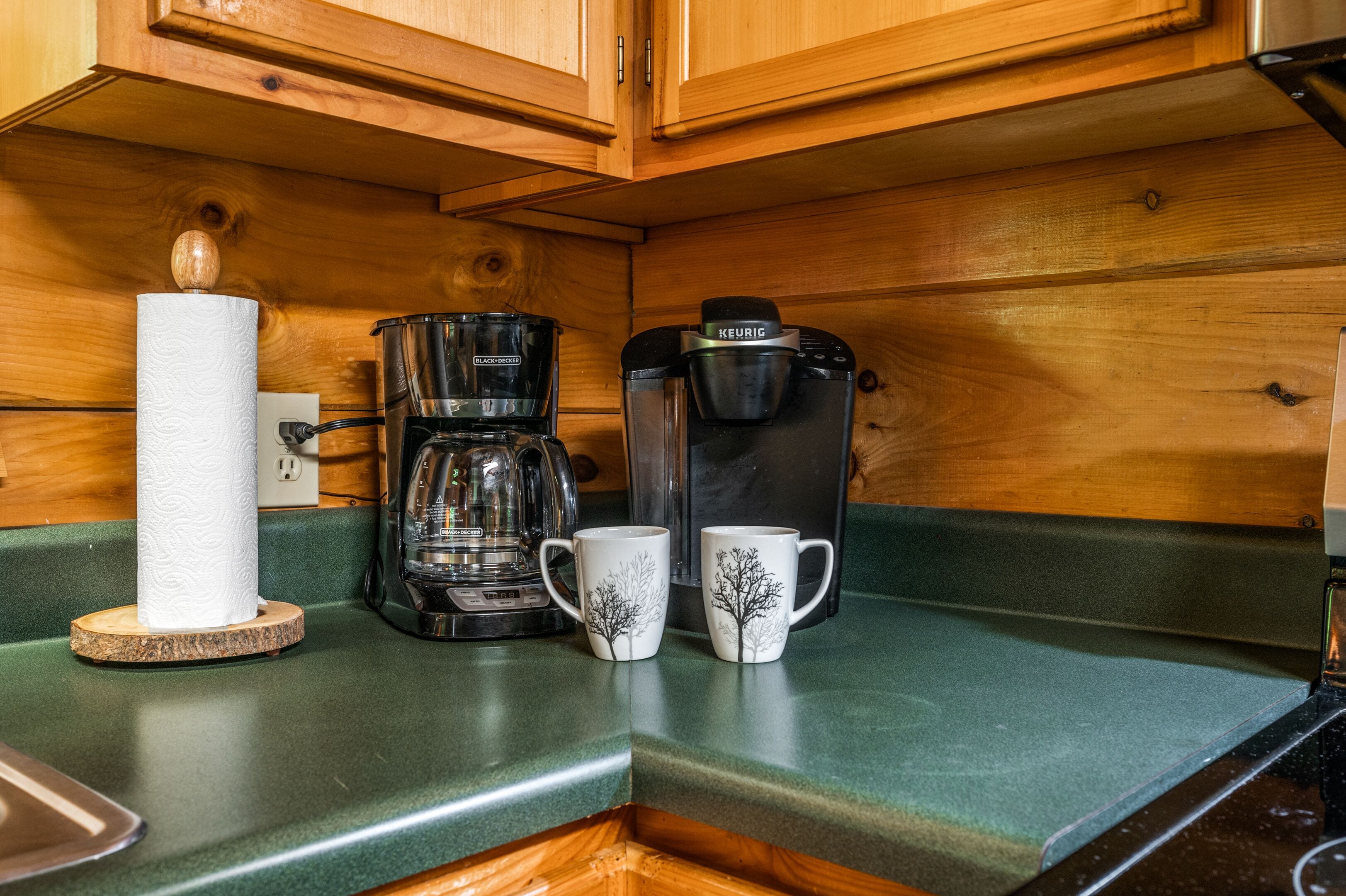 Un comptoir de cuisine avec une machine à café, deux tasses et un rouleau d’essuie-tout.