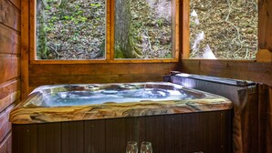 Una baita in legno con vasca idromassaggio, ampie finestre e vista sulla foresta.