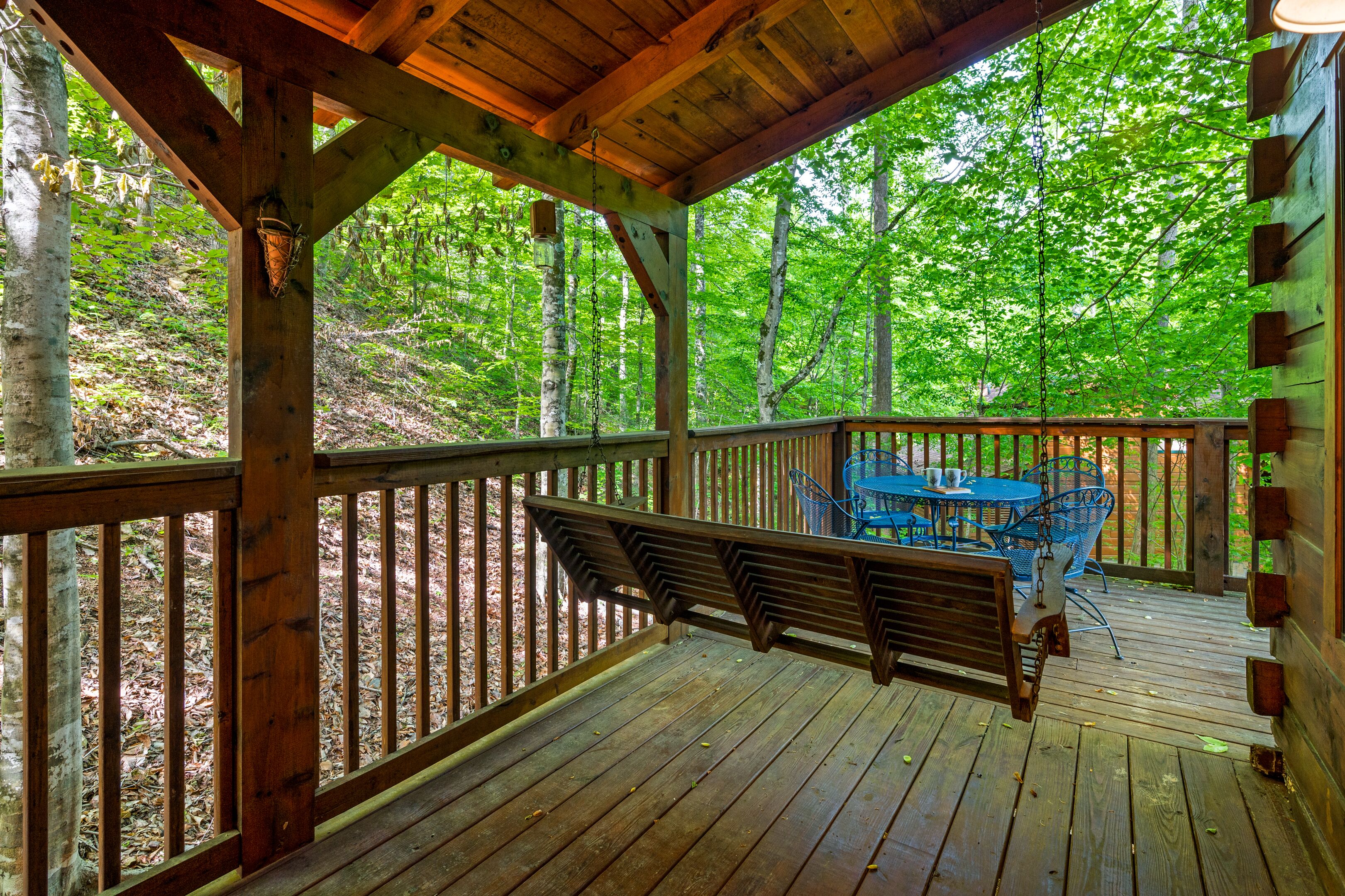 A wooden deck with a bench and a table, surrounded by trees.