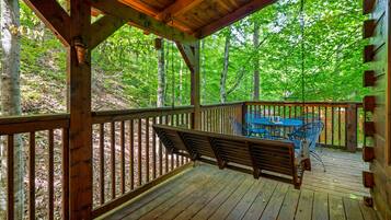A wooden deck with a bench and a table, surrounded by trees.