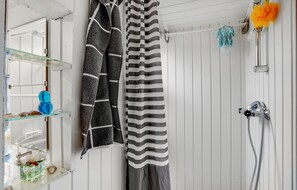 A bathroom with a shower, a glass shelf with toiletries, and striped towels hanging on the wall.