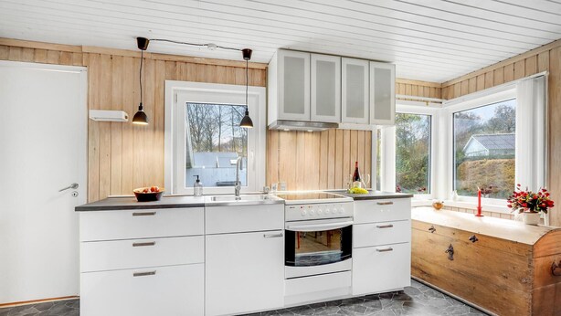 Une cuisine moderne avec des meubles blancs, un four encastré et une grande fenêtre donnant sur l’extérieur.