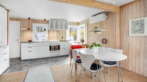 Une cuisine moderne avec des meubles blancs, un îlot central et un coin repas comprenant une table et des chaises blanches.