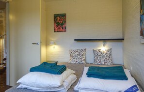 Ein kleines, sauberes Zimmer mit zwei Betten, jeweils mit Kissen und Handtuch. Eine Wandleuchte und ein Poster sind an der Wand angebracht.