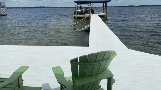A wooden pier extending into a lake with a covered dock area and green chairs.