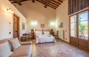 A cozy bedroom with a large bed, a wooden headboard, a desk with a lamp, and a view of the garden through a large window. - 1 bedroom nice home in Siena (Siena)