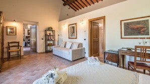 A spacious bedroom with a large bed, a sofa, a wooden desk, and a dining table. There are framed pictures on the walls and a bookshelf. - 1 bedroom nice home in Siena (Siena)