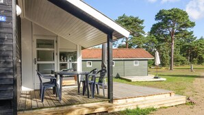 Une terrasse en bois avec une table et des chaises, un porche couvert et un petit abri de jardin, le tout situé dans un espace verdoyant avec des arbres.