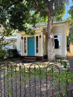 A single-story house with a front porch, a blue door, and a tree in front.