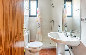 Bathroom features a toilet, sink, and shower area with a window above.