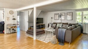 Ein modernes Wohnzimmer mit einer großen Couch, einem Couchtisch und einem Fernseher. An den Wänden befinden sich gerahmte Bilder und eine Uhr.