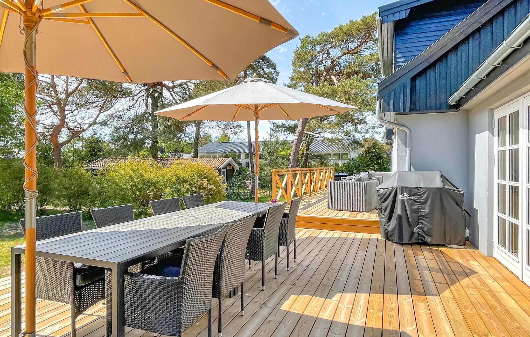 An outdoor deck with a table and chairs, a covered grill, and umbrellas.