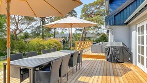 Eine Terrasse im Freien mit Tisch, Stühlen, einem Grillunterstand und Sonnenschirmen.