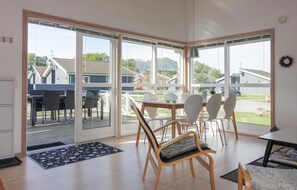 Una habitación amplia con ventanas grandes, una zona de comedor con sillas blancas y una mesa de madera.