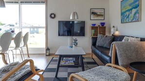 Ein Wohnzimmer mit Fernseher, einer Couch, Sesseln und einem Essbereich mit Tisch und Stühlen.