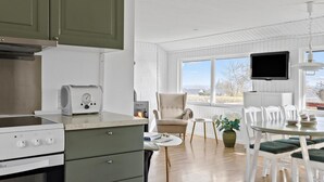 A modern kitchen with white appliances, a dining area with white chairs, a TV mounted on the wall, and a window with a view of the outdoors. - Beautiful home in Allinge with WiFi (Allinge)