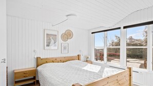 A bedroom with a wooden bed, a bedside table, a wall-mounted light, and a window with a view of the outdoors. - Beautiful home in Allinge with WiFi (Allinge)
