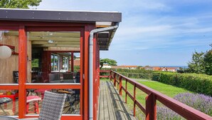A wooden deck with red railings, outdoor seating, and a view of the sea and houses. - Beautiful home in Allinge with WiFi (Allinge)