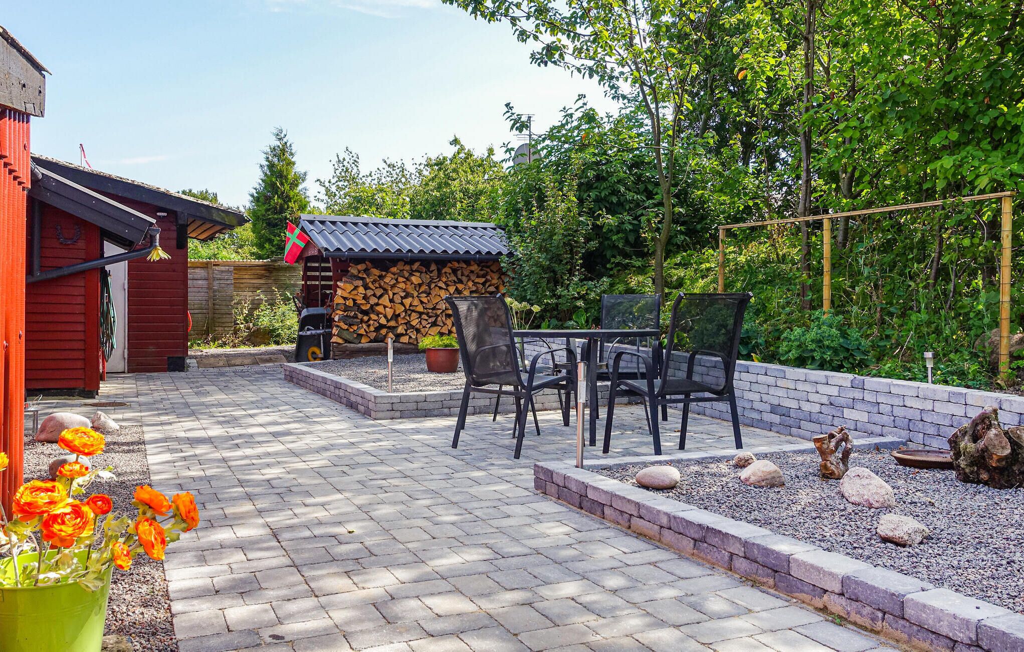A patio with a brick floor, a table with chairs, and a small shed with stacked firewood.