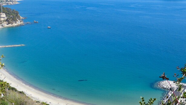 Blick auf die Küste mit blauem Meer, Sandstrand und einem Felsen mit einer Flagge.