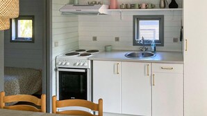 Una cocina compacta con armarios blancos, una estufa y un lavamanos. Hay dos ventanas que aportan luz natural y un pequeño estante sobre la estufa con utensilios de cocina.