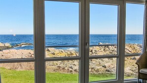 Una habitación con un amplio ventanal que da a un litoral rocoso y al mar.