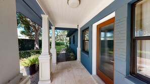 Guests can enjoy a covered porch with white columns and a ceiling, adjacent to a building with a brown-framed window.