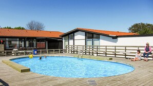 En swimmingpool med ett trädäck, en byggnad med ett rött tegeltak och en vit vägg med fönster.