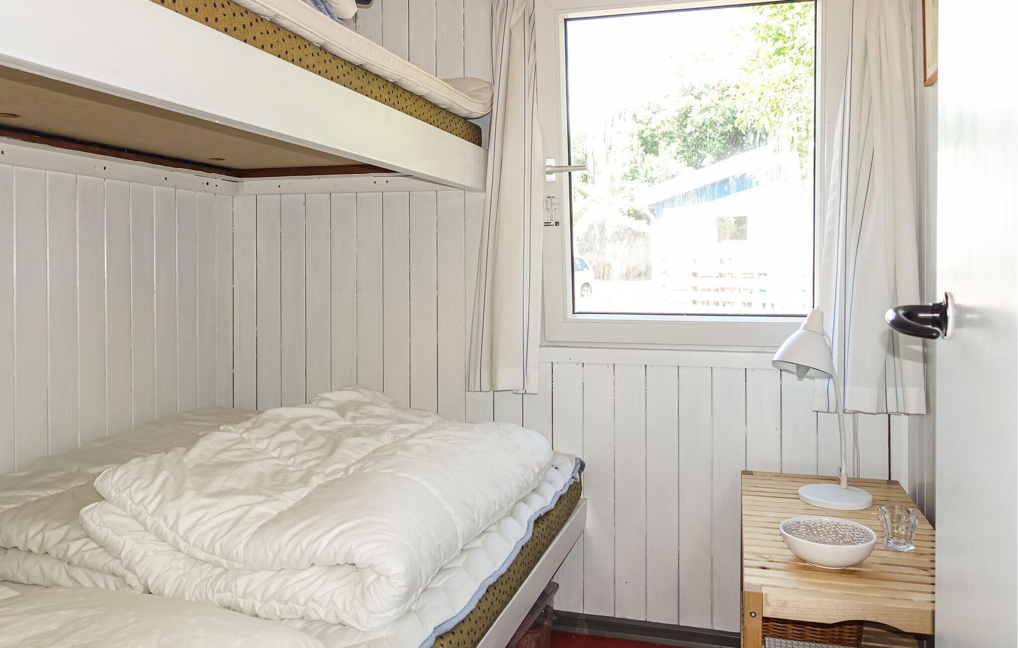 Un lit superposé avec un matelas blanc et une table en bois sur laquelle se trouvent un bol et un verre.
